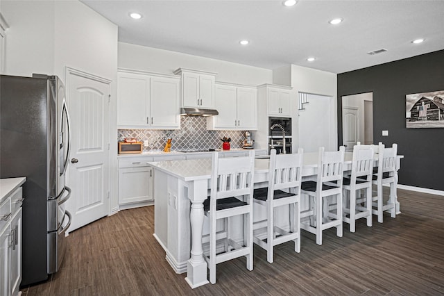 kitchen with stainless steel appliances, under cabinet range hood, dark wood-type flooring, visible vents, and backsplash