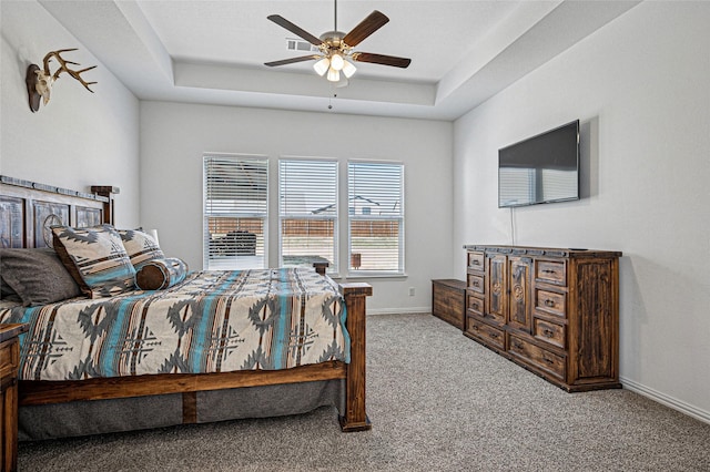 carpeted bedroom with a raised ceiling, ceiling fan, and baseboards