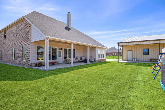 rear view of house featuring a patio area, a chimney, outdoor lounge area, a lawn, and roof with shingles