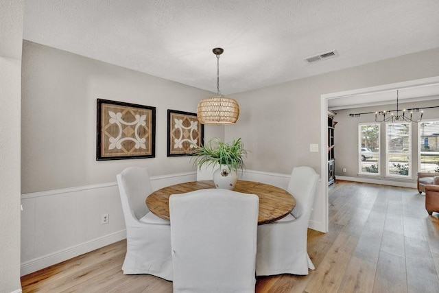 3509 Appalachian Ct, Plano, TX 75075 - dining space with a chandelier, light wood finished floors, a textured ceiling, and a wainscoted wall