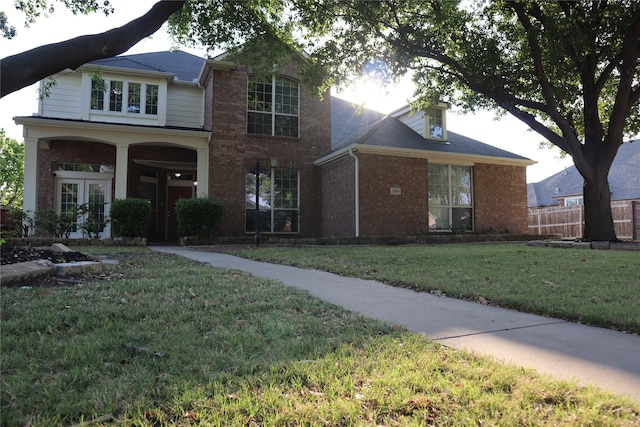 view of front facade featuring fence, french doors, a front yard, and brick siding