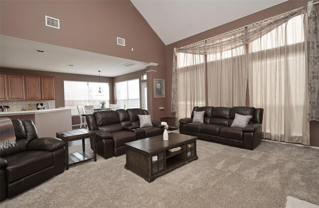 living area with light colored carpet, visible vents, and high vaulted ceiling