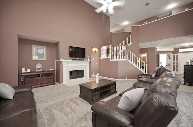 carpeted living area with a tiled fireplace, baseboards, a towering ceiling, stairway, and ceiling fan