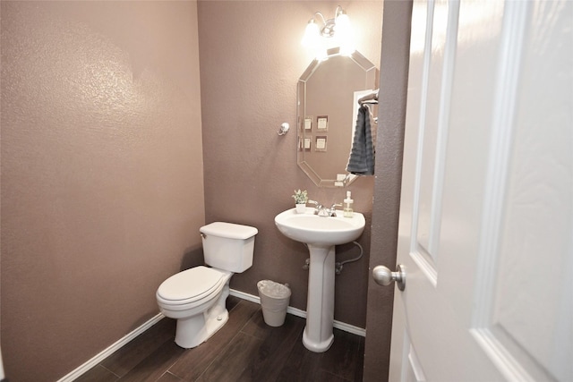 bathroom with baseboards, wood finished floors, a sink, and toilet