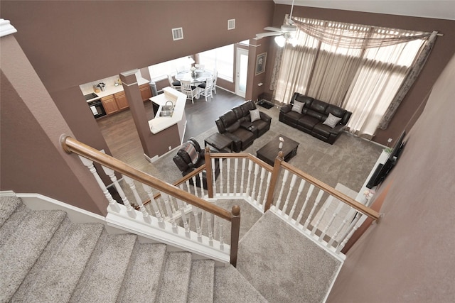 staircase featuring visible vents, a ceiling fan, a high ceiling, and carpet floors
