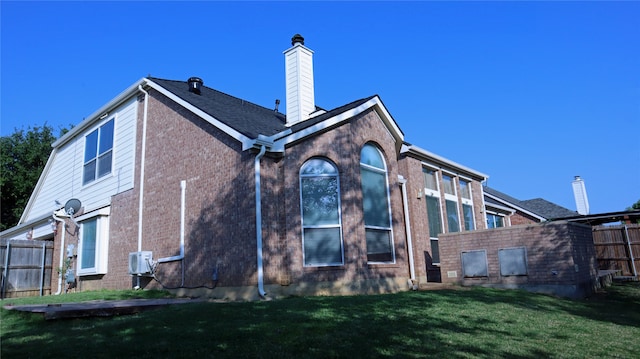 back of house featuring a lawn, brick siding, fence, and a chimney