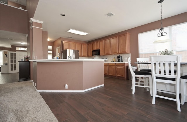 kitchen with light countertops, visible vents, black microwave, stainless steel fridge, and dark wood-style flooring