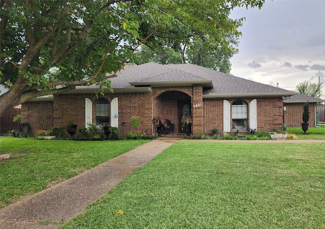 ranch-style home featuring brick siding, roof with shingles, and a front lawn