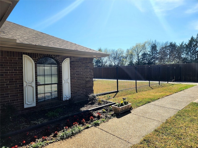 view of home's exterior featuring a lawn, brick siding, fence, and roof with shingles