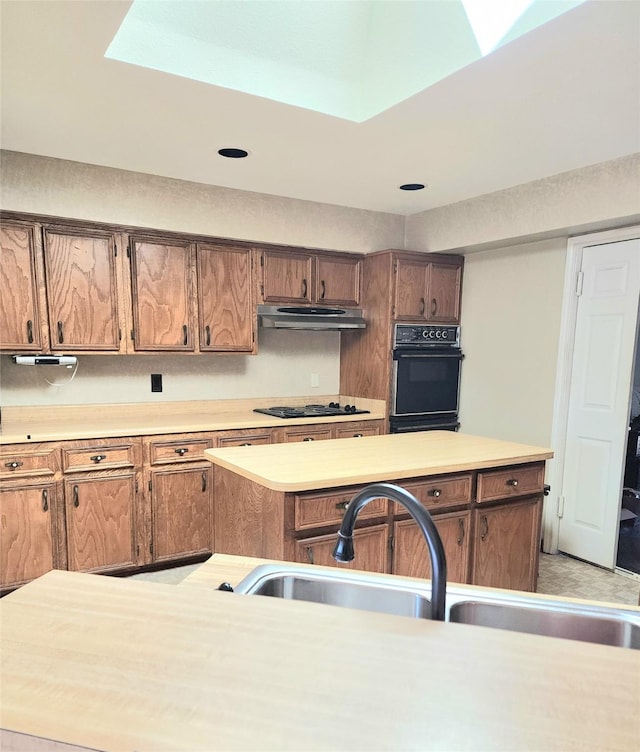 kitchen featuring light countertops, under cabinet range hood, black electric stovetop, and a sink