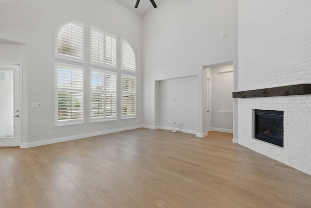 2205 Sandrellan St, Fort Worth, TX 76008 - unfurnished living room with a towering ceiling, light wood-type flooring, ceiling fan, a brick fireplace, and baseboards