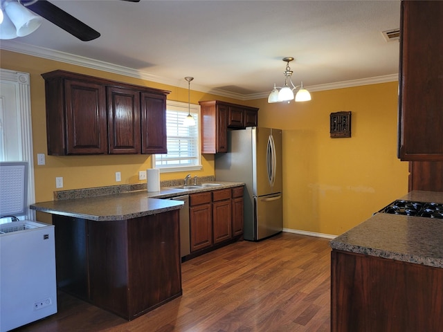 kitchen with dark wood-style floors, dark countertops, a sink, freestanding refrigerator, and a peninsula