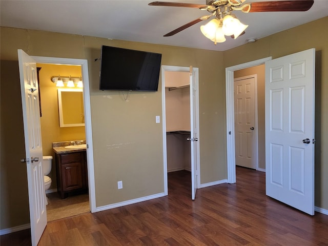 unfurnished bedroom featuring a spacious closet, wood finished floors, a sink, a closet, and baseboards