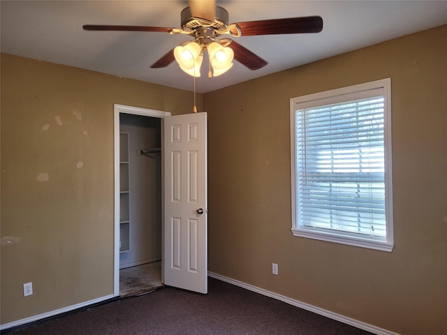 unfurnished bedroom featuring dark colored carpet, baseboards, a ceiling fan, and multiple windows