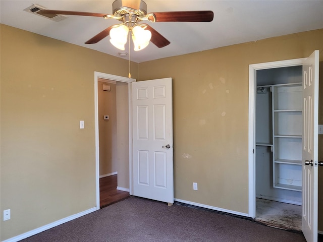 unfurnished bedroom with a closet, a spacious closet, dark carpet, baseboards, and visible vents