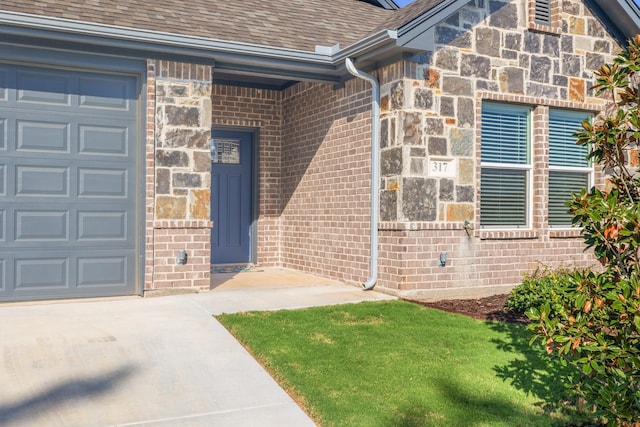 view of exterior entry with roof with shingles, a garage, driveway, and brick siding