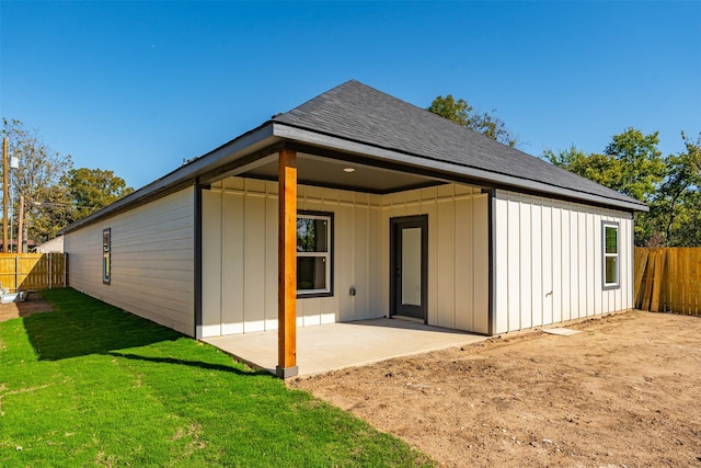 back of house with a patio area, a lawn, board and batten siding, a fenced backyard, and roof with shingles