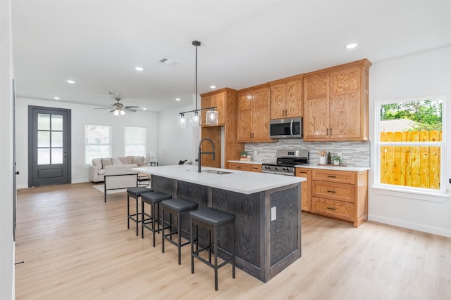 kitchen featuring decorative backsplash, a kitchen island with sink, light wood finished floors, appliances with stainless steel finishes, and visible vents