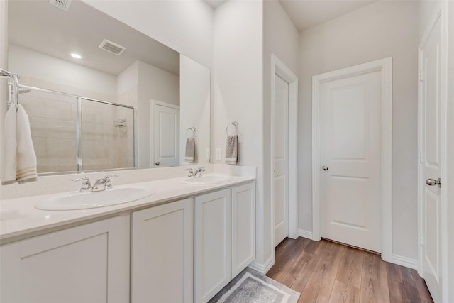 bathroom featuring visible vents, a shower stall, double vanity, wood finished floors, and a sink