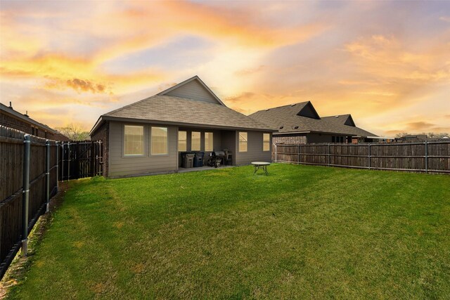 back of property at dusk featuring a fenced backyard, a lawn, and a shingled roof