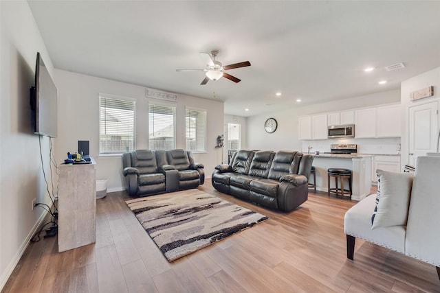 living room with light wood-style flooring, ceiling fan, visible vents, and recessed lighting