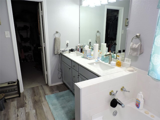 bathroom featuring a sink, wood finished floors, a spacious closet, a bath, and double vanity