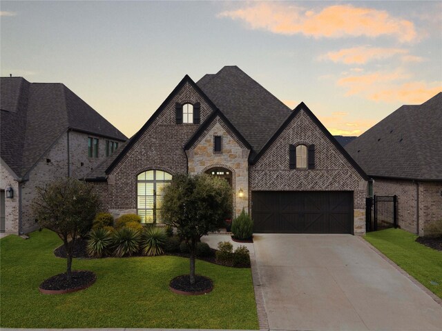french provincial home featuring a front lawn, driveway, stone siding, and brick siding