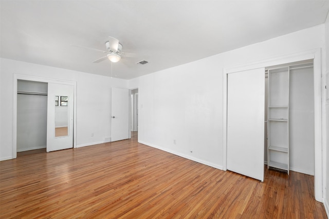unfurnished bedroom featuring light wood finished floors, baseboards, visible vents, and two closets