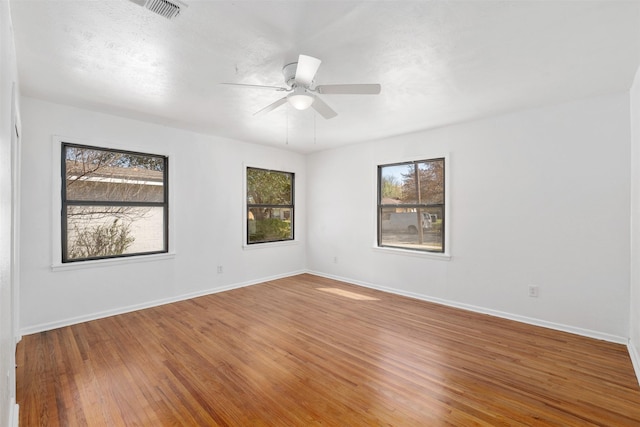 empty room with baseboards, visible vents, wood finished floors, and a ceiling fan
