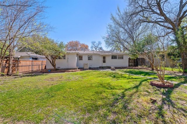 rear view of house with stucco siding, a fenced backyard, and a yard