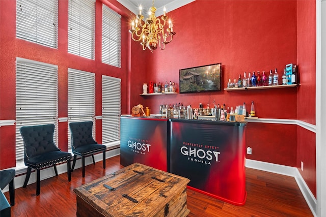 bar with a bar, baseboards, wood finished floors, and an inviting chandelier