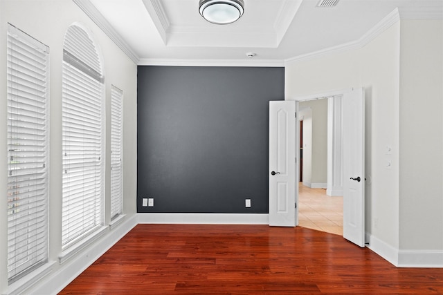 unfurnished bedroom with a tray ceiling, baseboards, wood finished floors, and ornamental molding