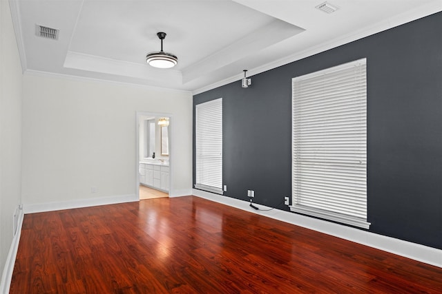 empty room featuring a raised ceiling, visible vents, baseboards, and wood finished floors