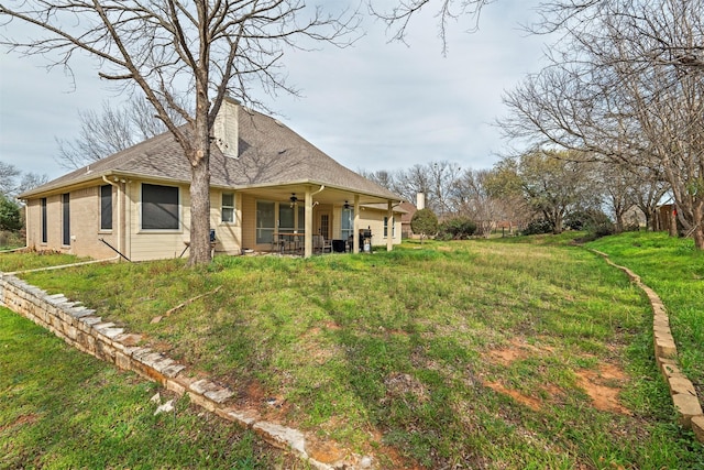 rear view of property with a patio, a chimney, a ceiling fan, roof with shingles, and a lawn