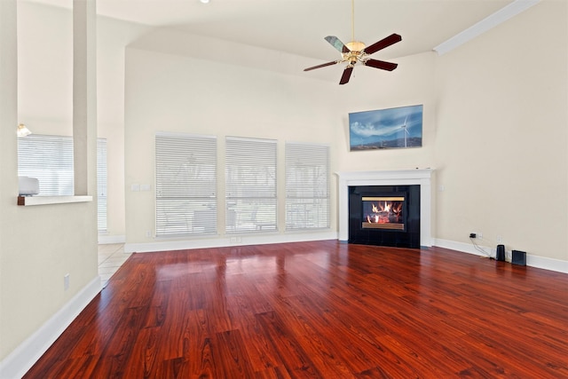 unfurnished living room featuring baseboards, ceiling fan, wood finished floors, and a tiled fireplace