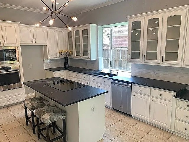 4726 Steeple Chase Ln, Rockwall, TX 75032 - kitchen featuring stainless steel appliances, dark countertops, light tile patterned floors, a kitchen bar, and ornamental molding