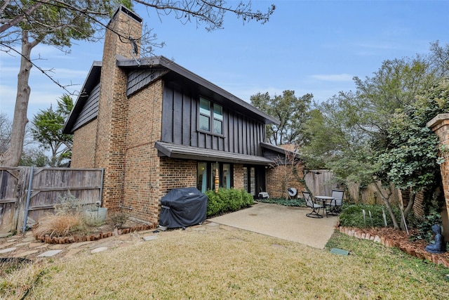 back of property featuring fence, a patio, brick siding, board and batten siding, and a lawn