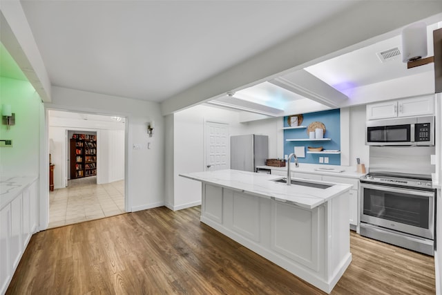 kitchen with an island with sink, a sink, stainless steel appliances, and wood finished floors