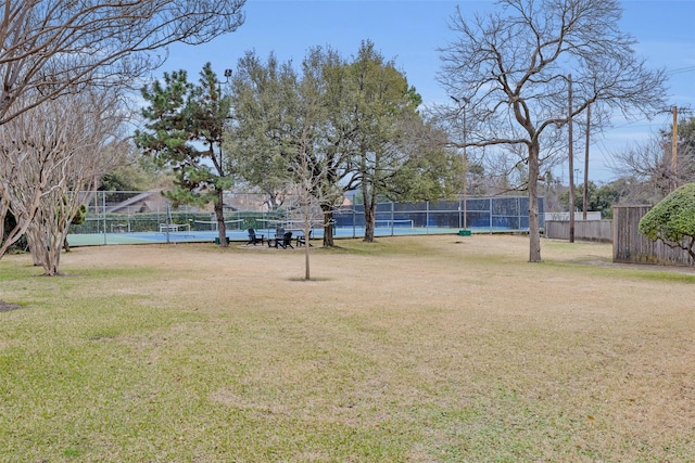 view of property's community featuring a tennis court, fence, and a yard