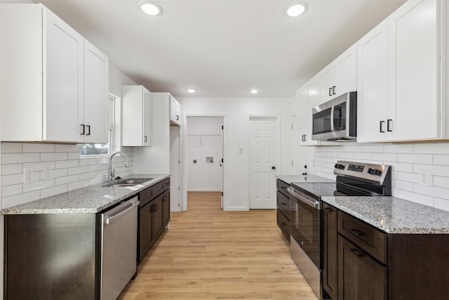 kitchen featuring light wood-style flooring, a sink, appliances with stainless steel finishes, and light stone countertops