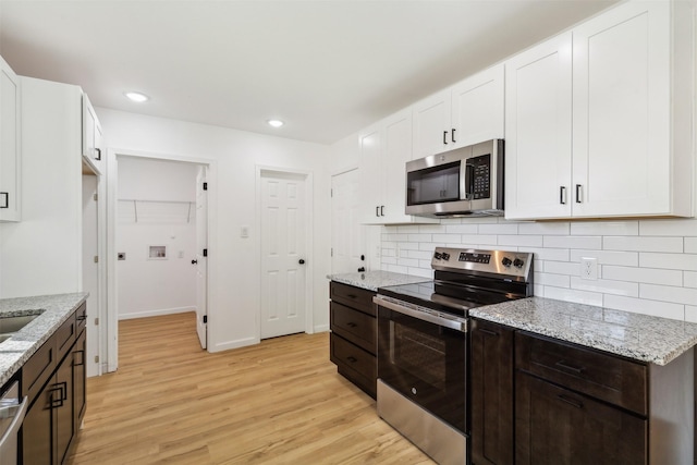 kitchen featuring backsplash, light stone counters, white cabinets, light wood-style flooring, and appliances with stainless steel finishes