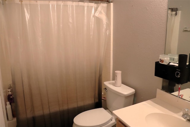 bathroom with toilet, vanity, a textured wall, and shower / bath combo with shower curtain