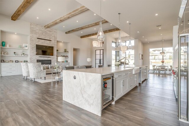 kitchen featuring a towering ceiling, white cabinets, wine cooler, a sink, and wood finished floors