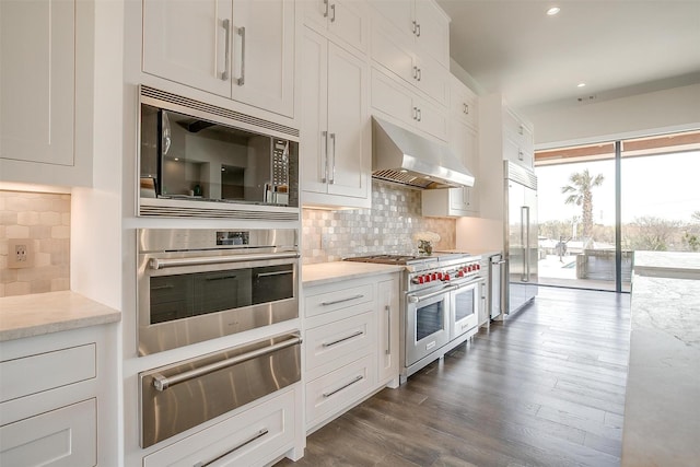 kitchen with white cabinets, a warming drawer, under cabinet range hood, dark wood-style flooring, and built in appliances