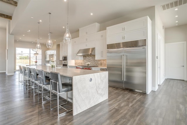 kitchen with tasteful backsplash, visible vents, under cabinet range hood, built in appliances, and a spacious island