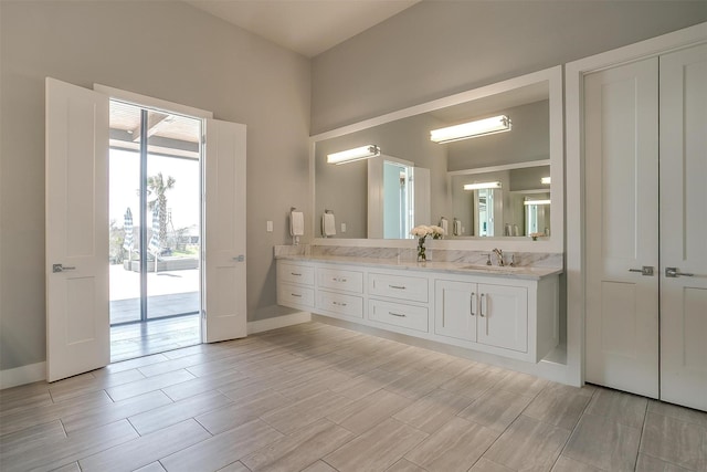 bathroom with wood finish floors, double vanity, a sink, and baseboards