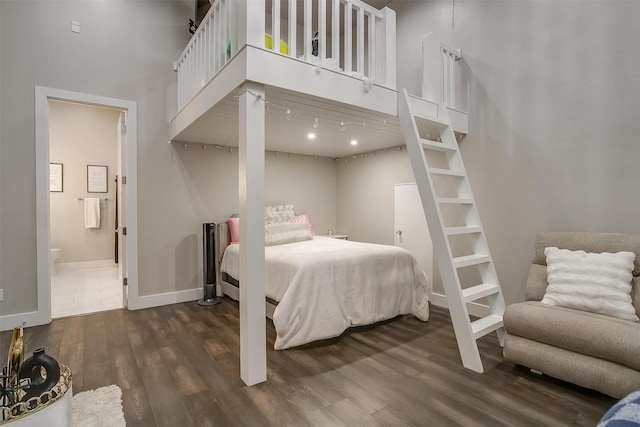 bedroom with a towering ceiling, baseboards, connected bathroom, and dark wood finished floors