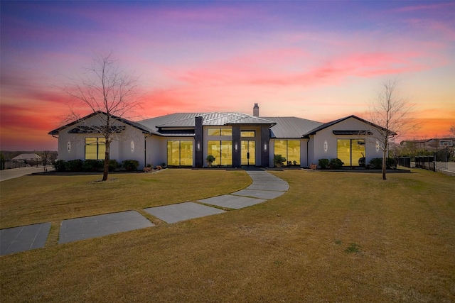 view of front of house with a front yard, solar panels, metal roof, a chimney, and stucco siding