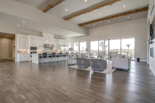 unfurnished living room featuring beamed ceiling, dark wood finished floors, recessed lighting, a high ceiling, and baseboards