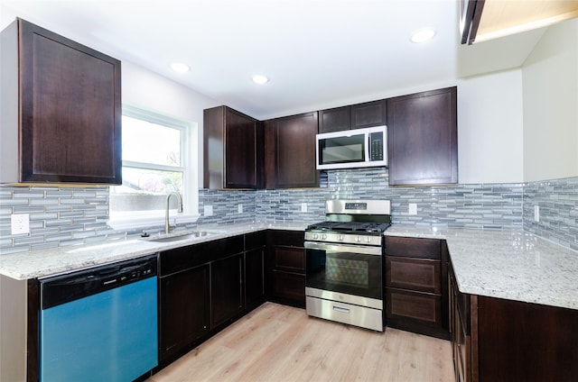 kitchen featuring light wood finished floors, stainless steel appliances, dark brown cabinets, a sink, and light stone counters